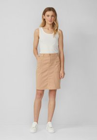 Beige katoenen rok met twee voorzakken, een rechte snit en een knoopsluiting. Gecombineerd met een wit geribd tanktop en witte sneakers.