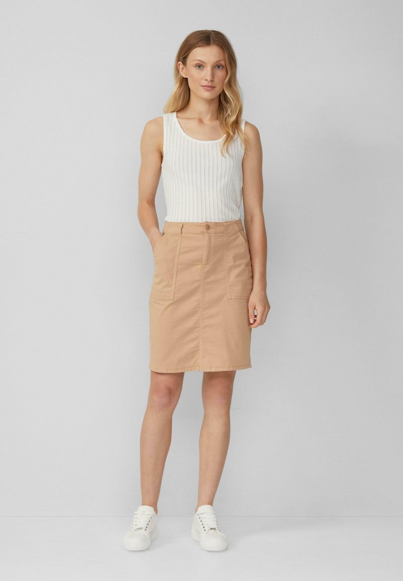 Beige katoenen rok met twee voorzakken, een rechte snit en een knoopsluiting. Gecombineerd met een wit geribd tanktop en witte sneakers.