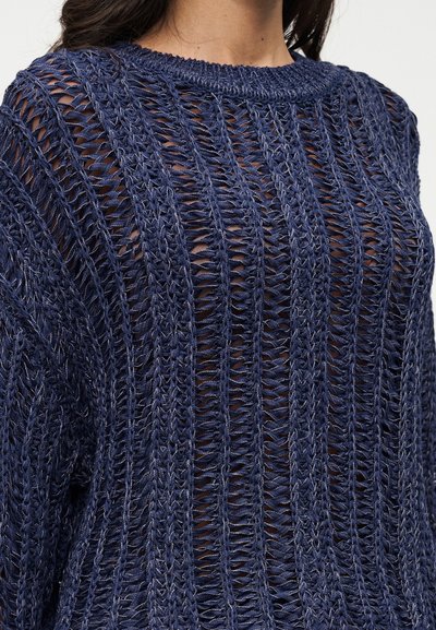 Pull en maille bleu marine avec un motif de points ouverts. Il présente un col arrondi et des manches amples, mettant en valeur sa texture respirante.