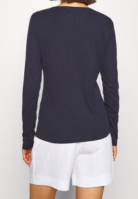 Navy long-sleeve top made of cotton, featuring a simple crew neckline and a fitted design, paired with white linen shorts.
