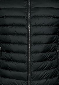 Chaqueta acolchada negra con diseño de rombos, presenta un cierre central con cremallera y dos bolsillos laterales con cremallera. Material resistente al agua.