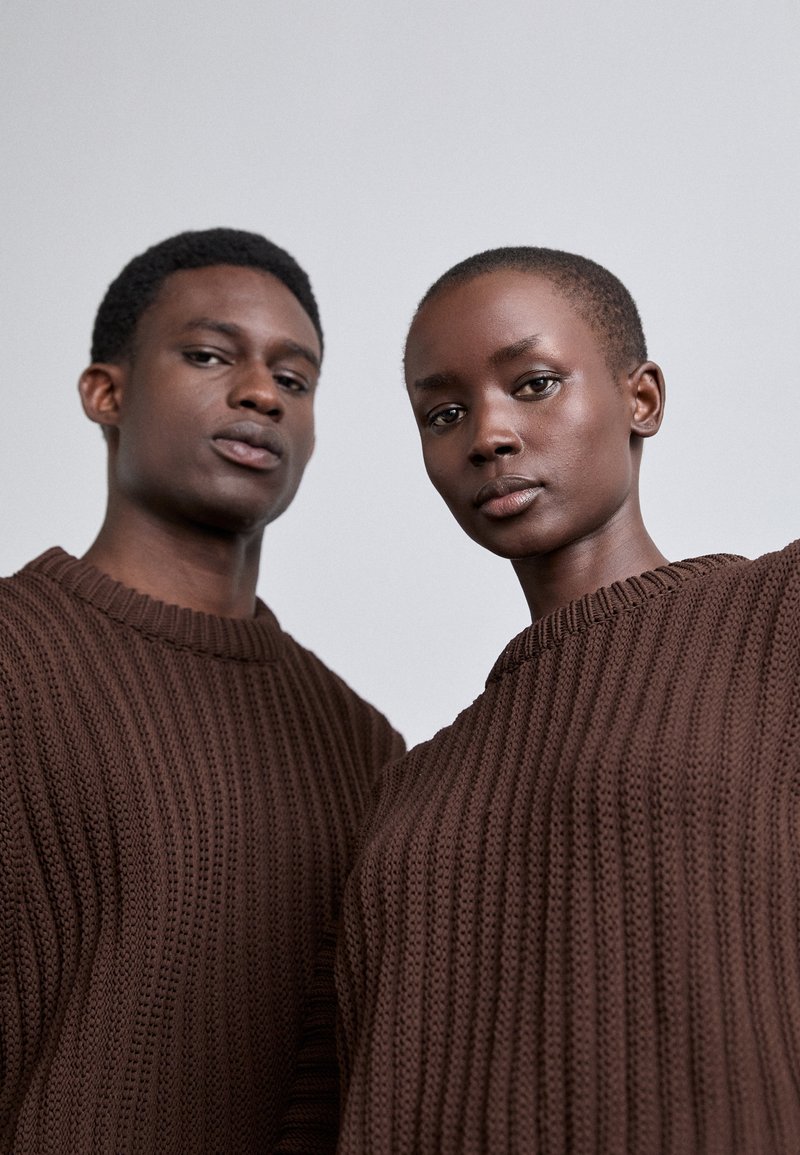 Brown knitted sweaters with a ribbed texture, featuring a wide neckline and long sleeves, worn by two models.