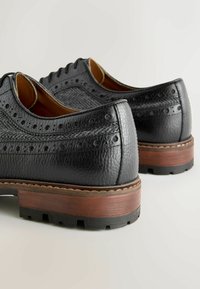 Black leather shoes with brogue detailing, featuring textured upper, round toe, and a contrasting brown and black sole.