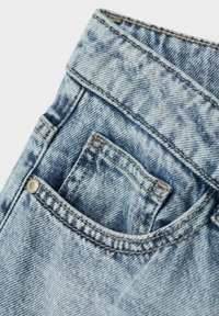 Jeans en denim avec un délavage bleu clair, des coutures visibles, une petite poche avant et un accent en rivet métallique près de la taille.
