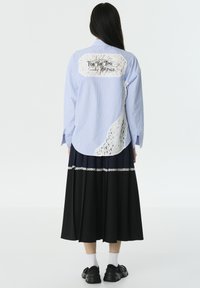 Blauw-wit gestreepte shirt met kantaccent en de tekst "For The Time Beings" op de achterkant. Gecombineerd met een zwarte plissérok en sneakers.