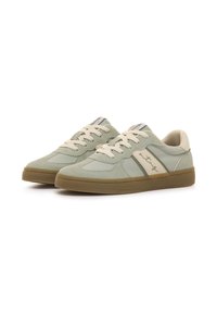 Par de zapatillas deportivas de ante verde claro y tela con cordones beige, franjas laterales en crema y suelas de goma color caramelo sobre un fondo blanco.