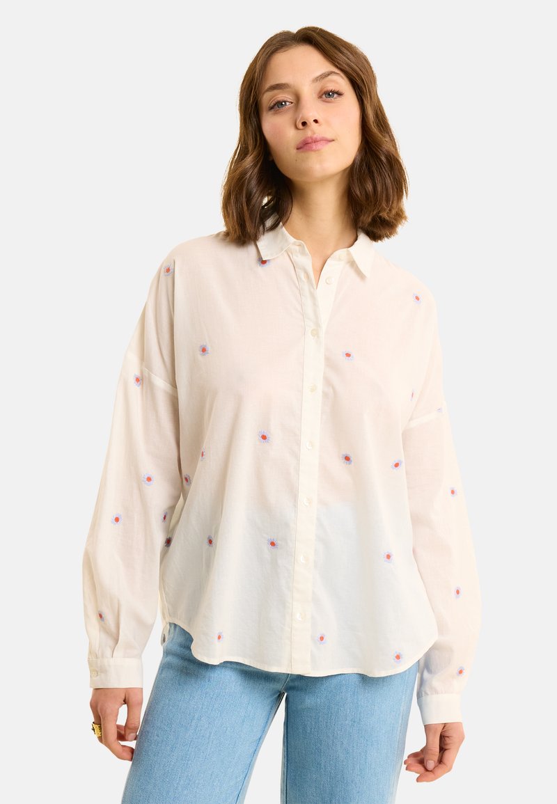 Camicia bianca a maniche lunghe con colletto a bottoni, decorata con piccoli fiori ricamati in rosso e blu. Tessuto morbido e leggero con una vestibilità comoda.