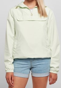 Lys grøn pulloverjakke med halve lynlås, elastiske manchetter, justerbar hætte og sidelommer. Parret med denimshorts.