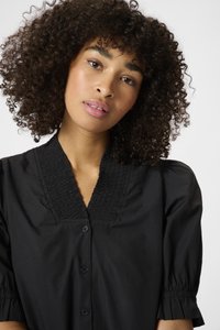 Zwarte blouse met knoopsluiting, een gesmokte halslijn, korte pofmouwen en een gladde textuur. Heeft een ontspannen pasvorm en een subtiele glans.