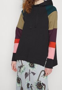 Felpa con cappuccio a blocchi di colore, corpo nero e dettagli in verde, marrone, viola, rosso e rosa. Caratterizzata da un cappuccio con lacci e maniche ampie.