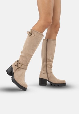 Botas de ante beige hasta la rodilla con un diseño arrugado, cremallera lateral, detalles de hebilla ajustable y un tacón grueso negro con una suela texturizada.