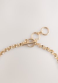 Gold-colored metal chain featuring interlinked oval links, with a smooth texture and a secure closure composed of circular rings.
