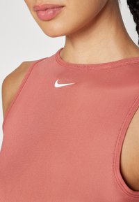 Ροζ αμάνικο αθλητικό μπλουζάκι με στρογγυλή λαιμόκοψη και μικρό λευκό λογότυπο Nike στο στήθος, φτιαγμένο από ομαλό, εφαρμοστό ύφασμα.