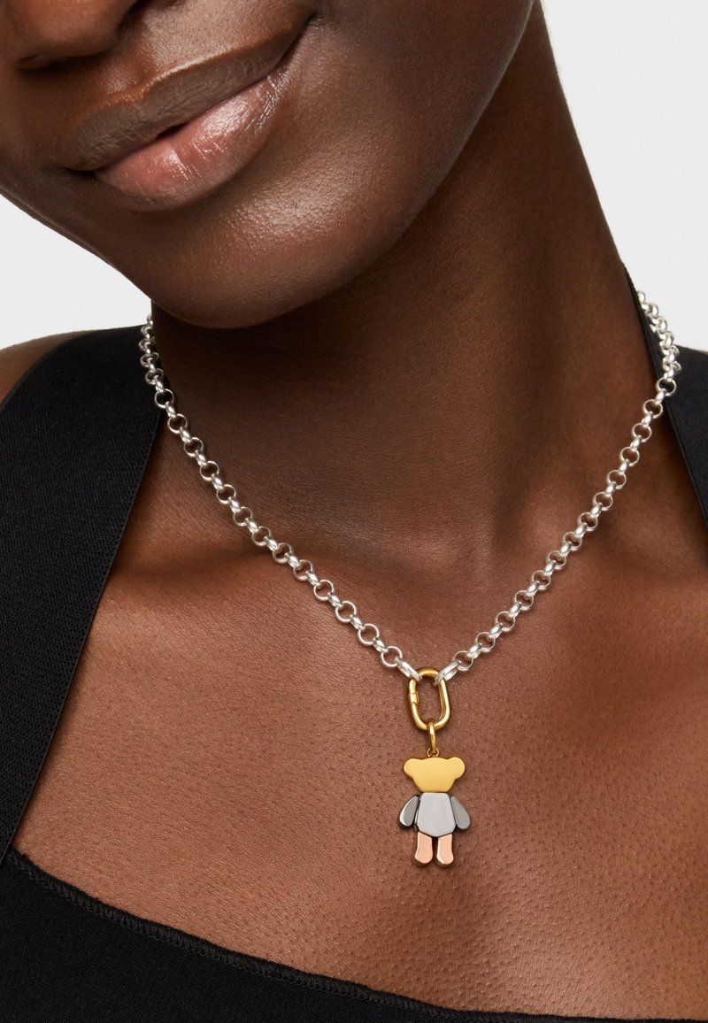 Collar de cadena de eslabones de plata con un cierre dorado y un charm de oso multicolor que presenta acentos en amarillo, gris, rosa y blanco.