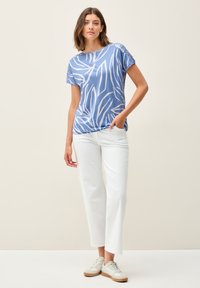 Haut court à manches courtes bleu avec des motifs de feuilles blanches, en tissu léger, col rond ; associé à un pantalon blanc court et des baskets beiges.