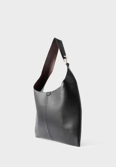 Μαύρη δερμάτινη τσάντα ώμου με φαρδιά λουράκι και ασημένια αγκράφα, εμφανιζόμενη σε απλό ανοιχτό φόντο.