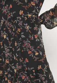 Zwarte bloemenjurk met levendige gele en rode bloemen en groene bladeren. De stof is lichtgewicht en heeft tiered ruffles.