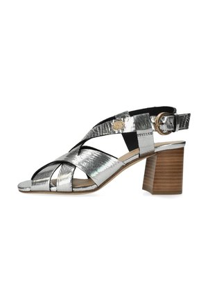 Zilverkleurige metallic sandalen met hak, voorzien van een kruisbanddesign, open teen, zwarte accenten en een bruine blokhak met textuur.