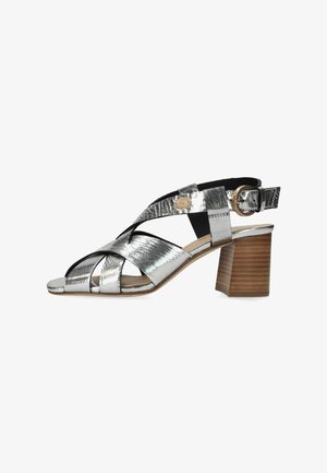 Sandalias metálicas plateadas con tacón, diseño de tiras cruzadas, punta abierta, detalles en negro y tacón tipo bloque marrón texturizado.