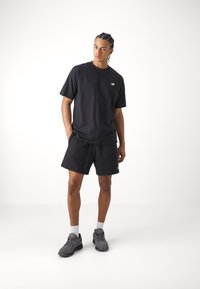 Black cotton t-shirt with short sleeves and a small logo, paired with black cotton shorts. Worn with gray sneakers and white socks.
