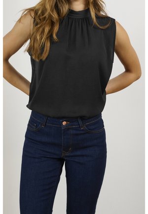 Schwarzes ärmelloses Oberteil mit plissiertem Ausschnitt, kombiniert mit dunkelblauen Jeans mit braunen Nähten und einer Knopfleiste vorne.