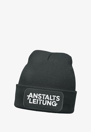Black ribbed beanie hat featuring a folded cuff and a prominent rectangular patch with white text “ANSTALTSLEITUNG.” Made from soft knit fabric.