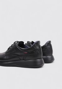 Zapatos de cuero negro con puntera redondeada, diseño con cordones, cuello acolchado y suela texturizada en contraste con acento de logo.