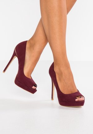 Pompes à talons hauts en daim bourgogne avec une ouverture au bout, un plateau et un talon aiguille élégant. Texture lisse et design découpé sur les deux côtés.