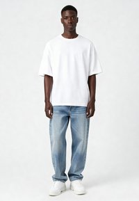 Balts kokvilnas T-krekls ar brīvu piegriezumu un apaļu kakla izgriezumu, apvienots ar gaiši ziliem džinsu biksēm un baltām sporta apavām. Vienkāršs un ikdienišķs dizains.