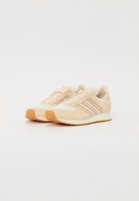Beige sportcipők velúr és hálós felsőrésszel, három vízszintes csikozással és mintás gumitalppal.
