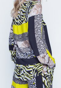 Pitkähihaisen paidan kuosina eläinkuoseja ja kirkkaan keltaisia yksityiskohtia tummalla pohjalla; pehmeä kangas ja rento istuvuus.