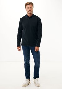 Polo shirt nero a maniche lunghe con colletto, abbinato a jeans blu e sneakers bianche. Presenta un logo discreto sul petto.