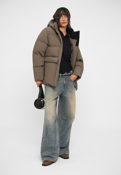 Puffer jacket in taupe with a hood and front pockets, paired with faded blue wide-leg jeans and a round black bag.