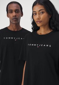 Le t-shirt neri in cotone presentano il logo "TOMMY JEANS" in bianco con un piccolo accento colorato. Il design ha maniche corte e collo a giro.