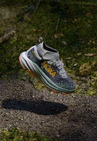 Scarpa da corsa leggera con tomaia grigia e accenti neri e verdi, suola ammortizzata e superficie testurizzata con dettagli di allacciatura e logo.