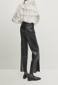 Blusa bianca a strati e sbuffi abbinata a pantaloni in pelle neri a vita alta. Il look è completato da scarpe basse nere e un design semplice.