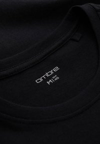 Gros plan du col d'un T-shirt noir avec une étiquette de taille blanche imprimée « ombre M1 eur 48 » à l'intérieur du col.