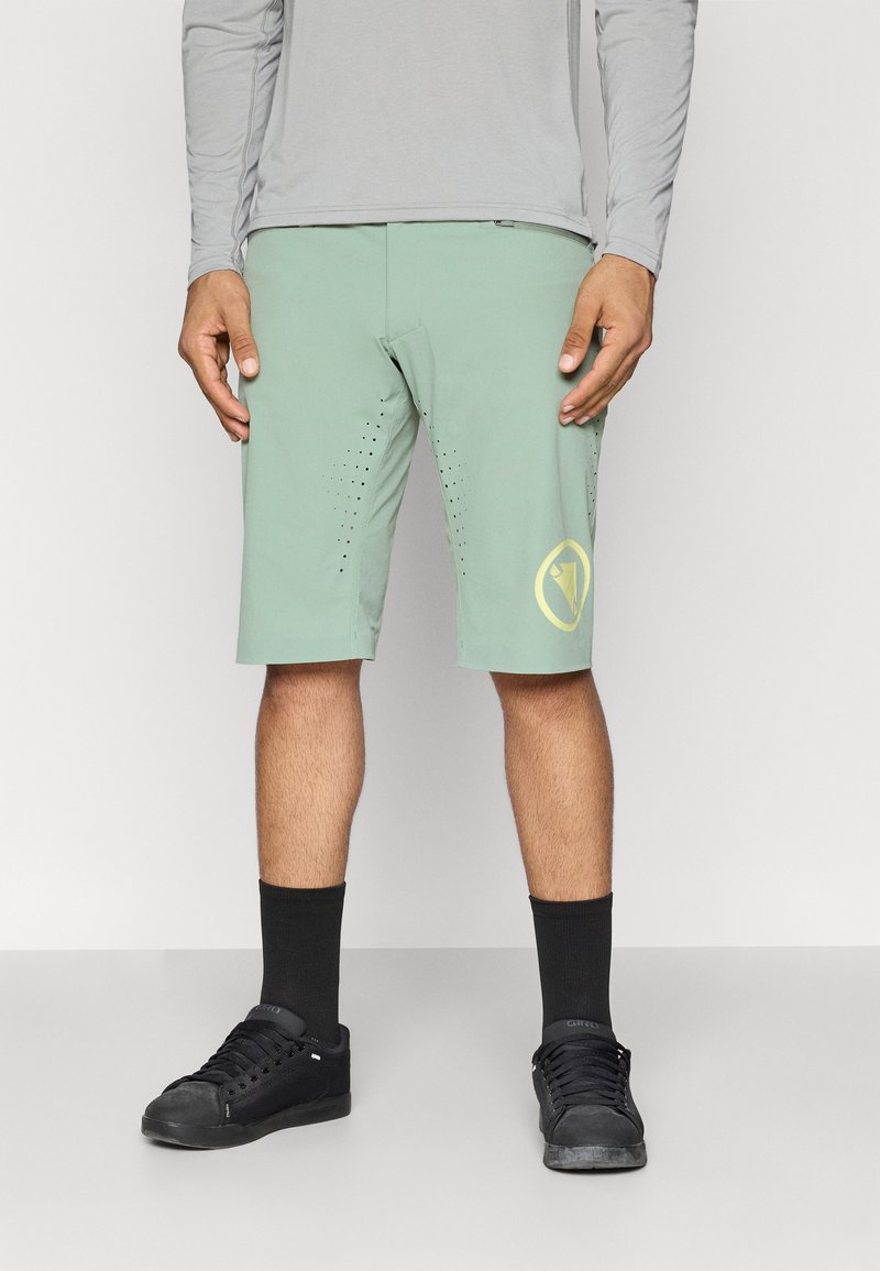 Svijetlozelene kratke hlače s perforiranim detaljima sa strane, s žutim logotipom. Crne čarape i cipele upotpunjuju odjevnu kombinaciju.