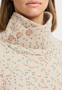 Top beige con colletto alto caratterizzato da un motivo a pois multicolore in blu, arancio e bianco; tre bottoni decorativi sul colletto.