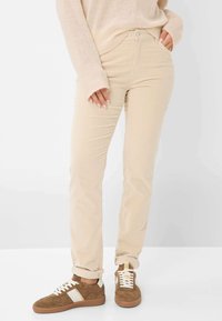 Beige Cordhosen mit passgenauer Silhouette, ausgestattet mit einem Reißverschluss, zwei vorderen Taschen und umgeschlagenen Säumen, kombiniert mit braunen Wildledersneakern.