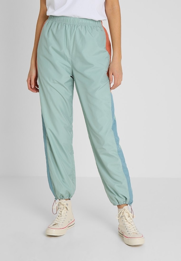 Lätta, pastellgröna träningsbyxor med elastisk midja, som har blå och orange sidopaneler, samlade muddar och en avslappnad passform.
