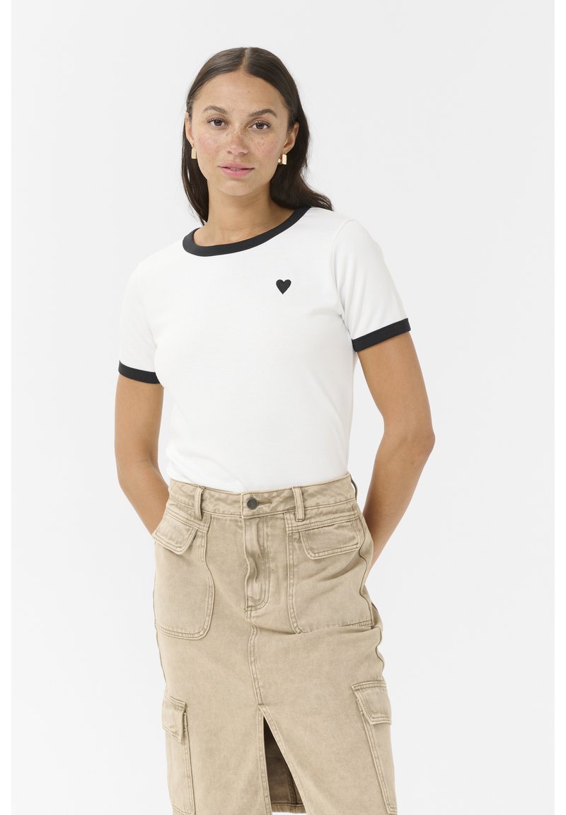 White short-sleeve t-shirt with black trim and small heart logo. Paired with a beige skirt featuring pockets and a front slit.