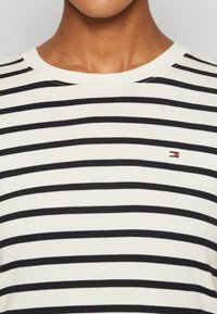 Pruhované bavlněné tričko s vodorovnými černobílými pruhy, kulatým výstřihem a malým logem na levé části hrudi.