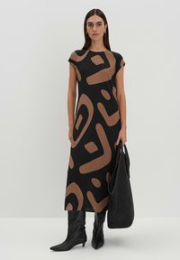 Schwarzes Kleid mit braunen geometrischen Mustern, knielang, mit kurzen Ärmeln, kombiniert mit einer gestrickten schwarzen Tasche und knielangen schwarzen Stiefeln.