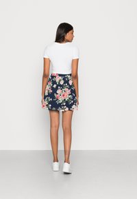 Top branco de manga curta combinado com uma saia floral azul-marinho com rosas cor-de-rosa e brancas. A modelo usa ténis brancos.