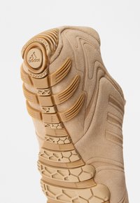 Bež sneakeri põhi tekstureeritud kummist, millel on kuhexagonaalsed mustrid ja tõstetud aktsendid. sisaldab "adidas" logo kontsas.