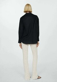 Camicia nera oversize con maniche lunghe, polsini con bottone e orlo dritto, abbinata a pantaloni a zampa d'elefante beige a coste e sandali.