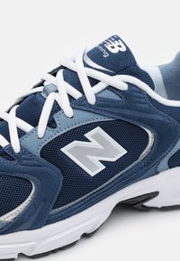 Mäns löparsko i marinblå mesh med blå och grå accenter, vita snören och gummisulor med en framtr ädande "N"-logotyp.