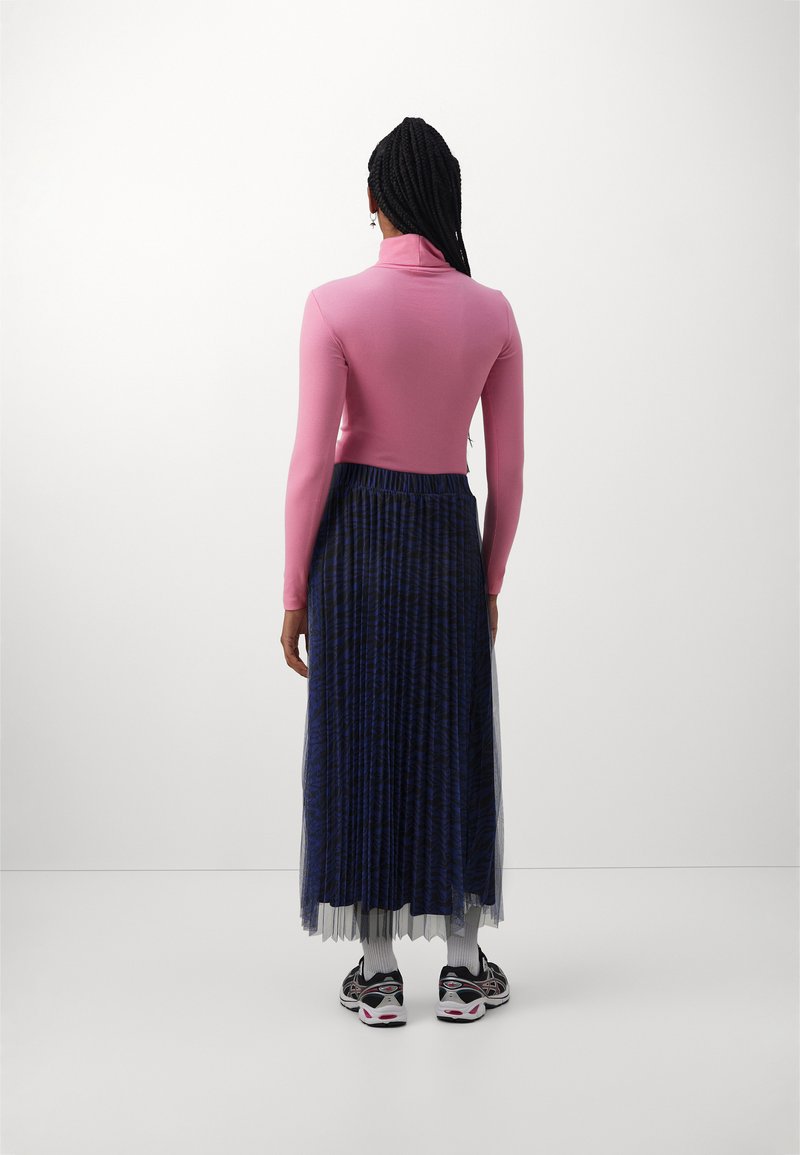 Roze langharige top met een hoge kraag, gecombineerd met een blauw geplooid rokje met een gestructureerd patroon, gedragen met zwarte sneakers en witte sokken.