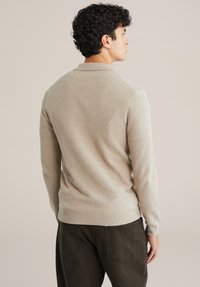 Bézs színű kötött pulóver hosszú ujjakkal és bordázott szegéllyel, strukturált felülettel. A dizájn klasszikus gallért és lazább szabást tartalmaz.